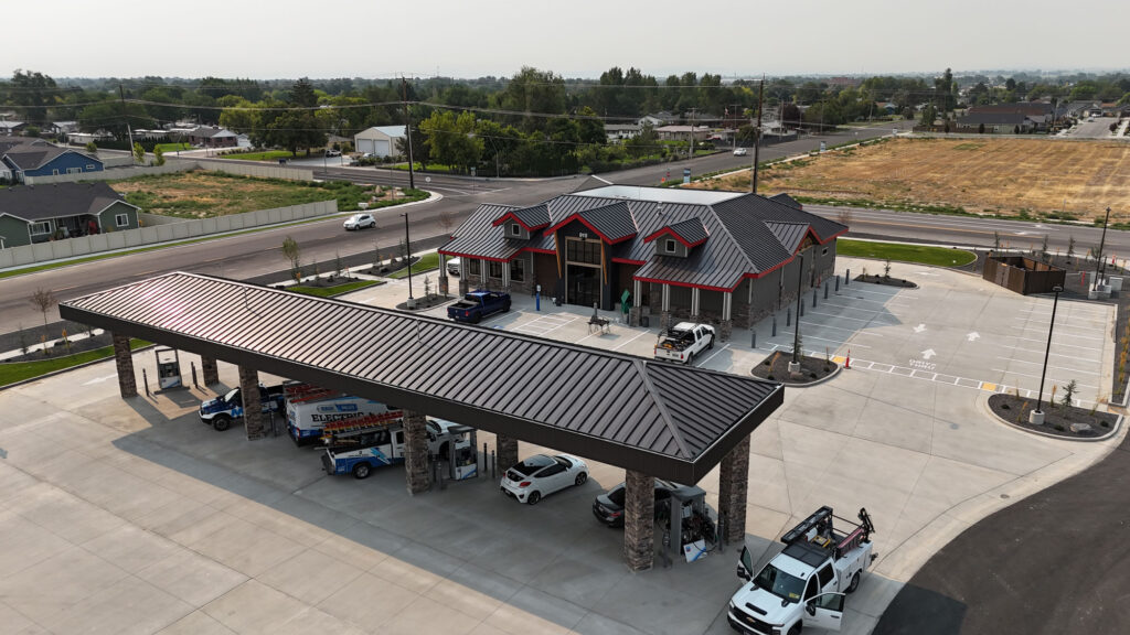 Aerial photo of an unfinished gas station. There is an employee working on one of the gas pumps and electrical trucks are in the parking spots.