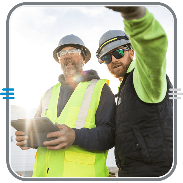 Two electrical technicians look at something in the distance just past the camera. One tech is holding a tablet.
