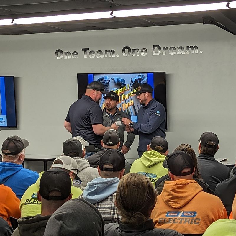 Photo of MVE team members at a meeting. Three men are discussing in front of a TV with the words "One Team. One Dream." written on the wall above.
