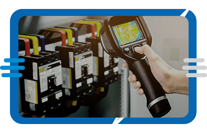 A person uses a handheld thermal imaging camera to inspect electrical components in a control panel, with colored wires and switches visible in the background.