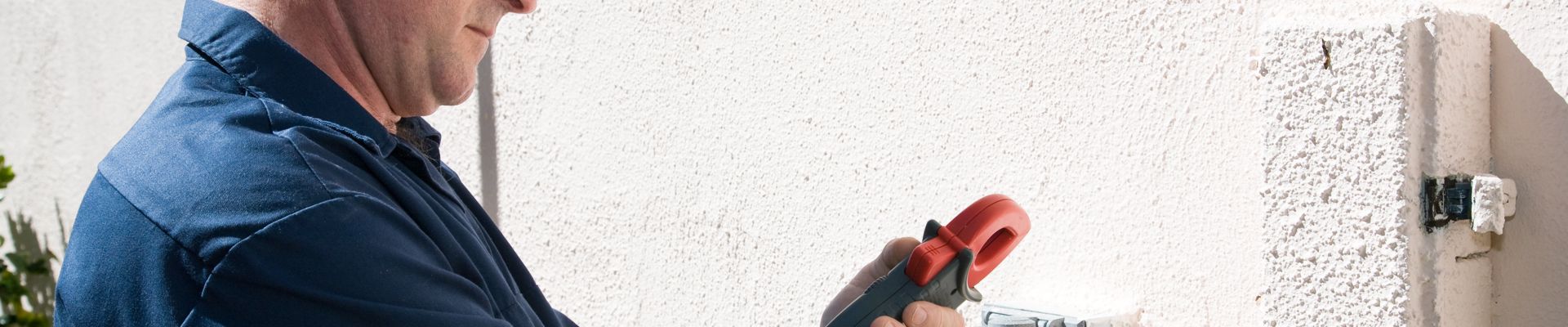 Man with electrical tool investigating outer wall outlet
